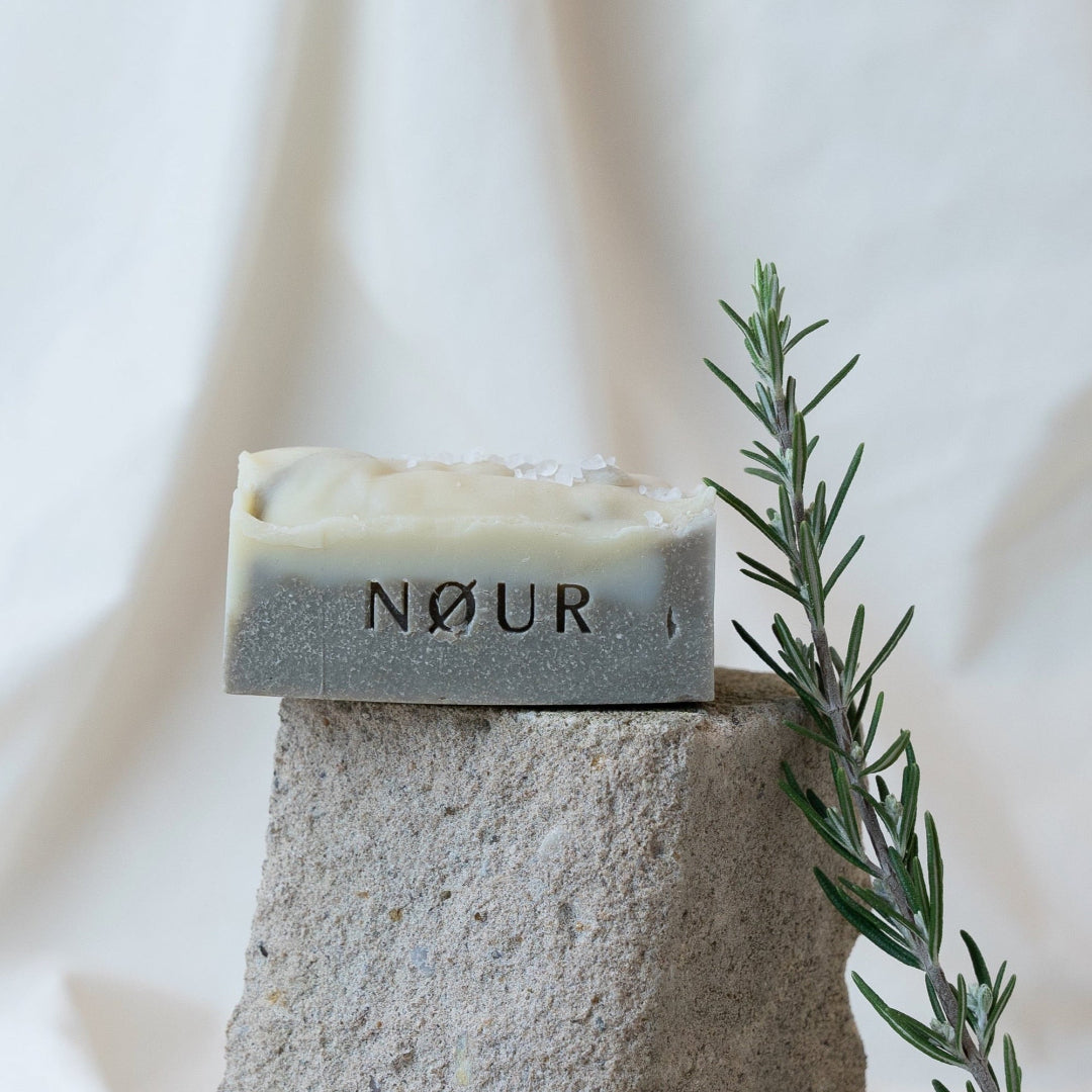 mud nour seife naturseife mit peelingeffekt bei unreiner haut bioseife dekoriert auf stein mit rosmarinzweig