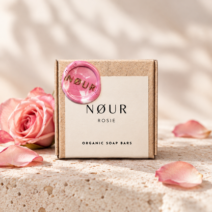 Verpackung von Rosie auf hellem Sandstein mit rosa Rosenblüte und -blättern