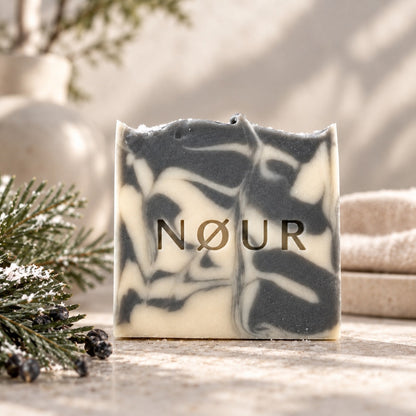 NØUR Naturseife Wintertime mit grau-weißer Marmorierung, dekoriert mit verschneiten Tannenzweigen, Wacholderbeeren und Handtuch