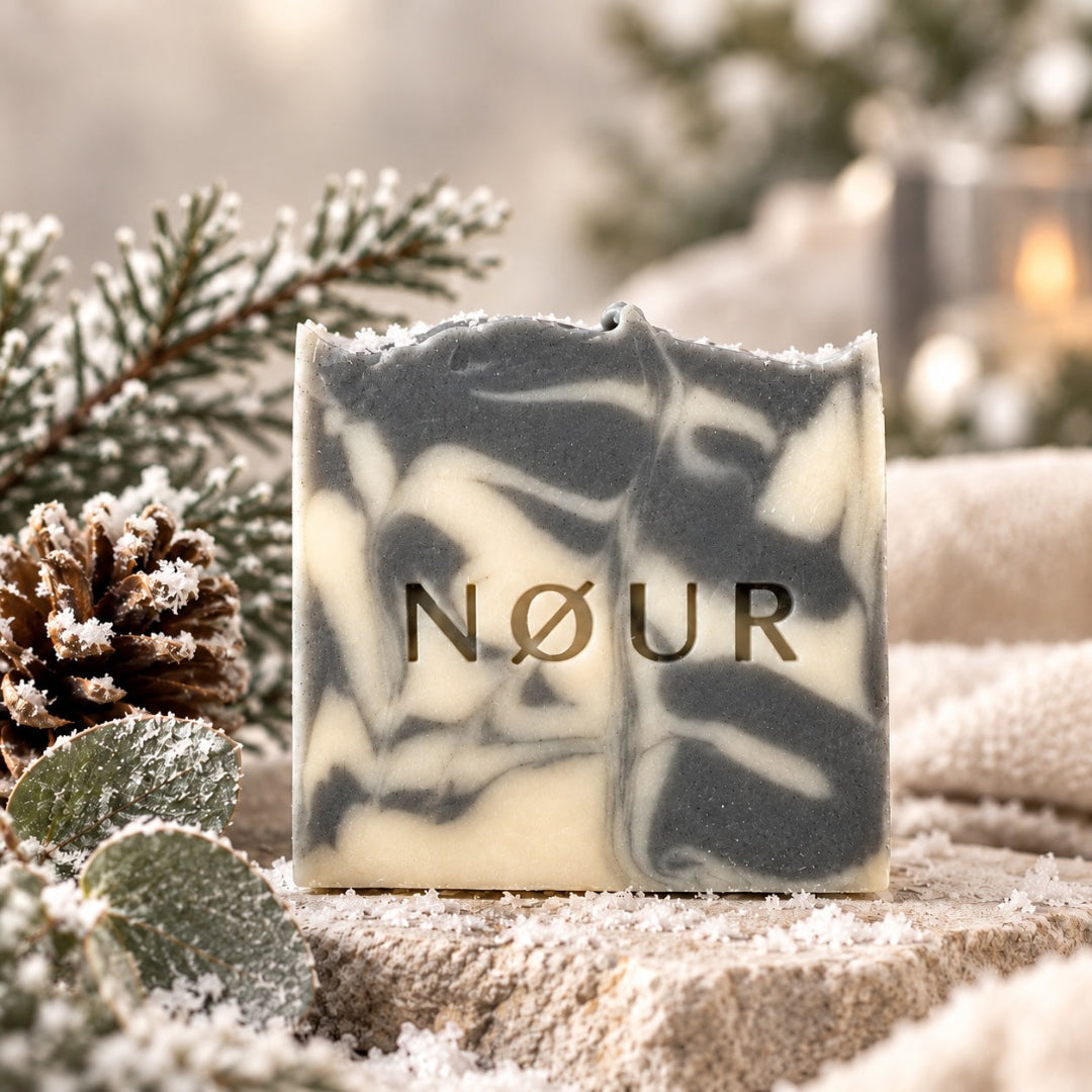 NØUR Naturseife Wintertime mit grau-weißer Marmorierung, winterlich dekoriert mit verschneiten Tannenzweigen und Tannenzapfen. 